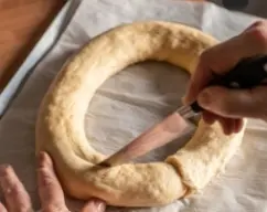 Step <p>Haz tres o cuatro cortes profundos hasta llegar al relleno de mazapán.</p><p>Cubre con un film transparente y deja fermentar hasta que doble su tamaño.</p> illustration