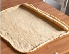 Step <p>Pon el cilindro de mazapán en el extremo mas ancho de la masa y envuelve con la masa.</p> illustration